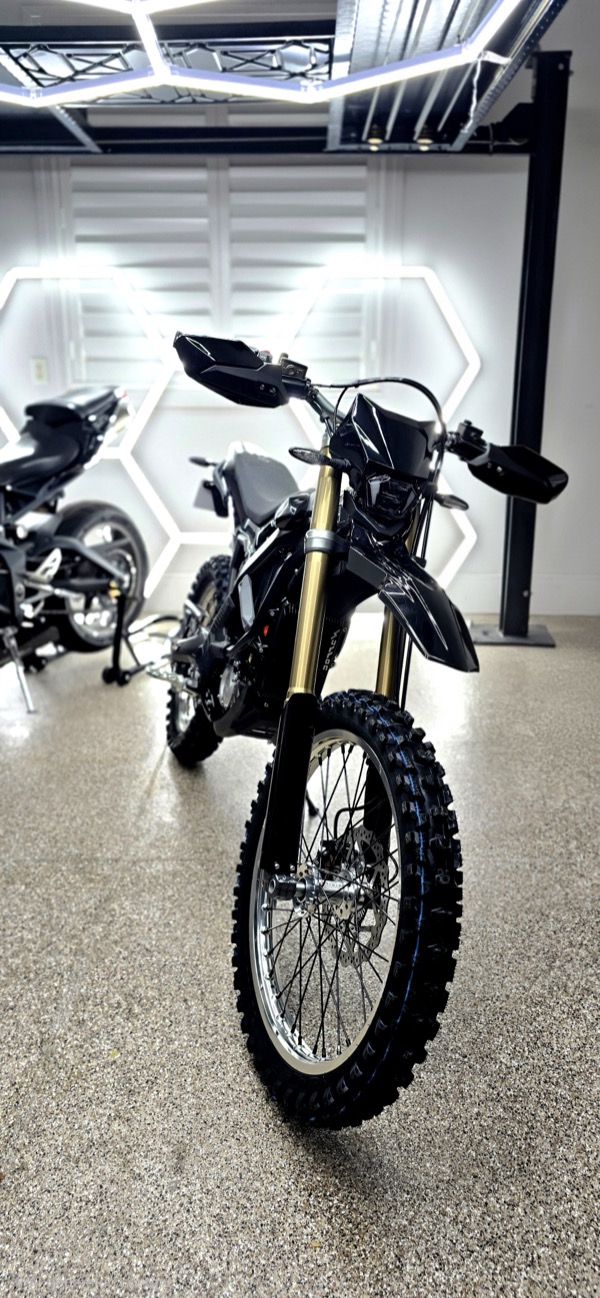 Front view of a black electric dirt bike in the Tuff Emoto garage